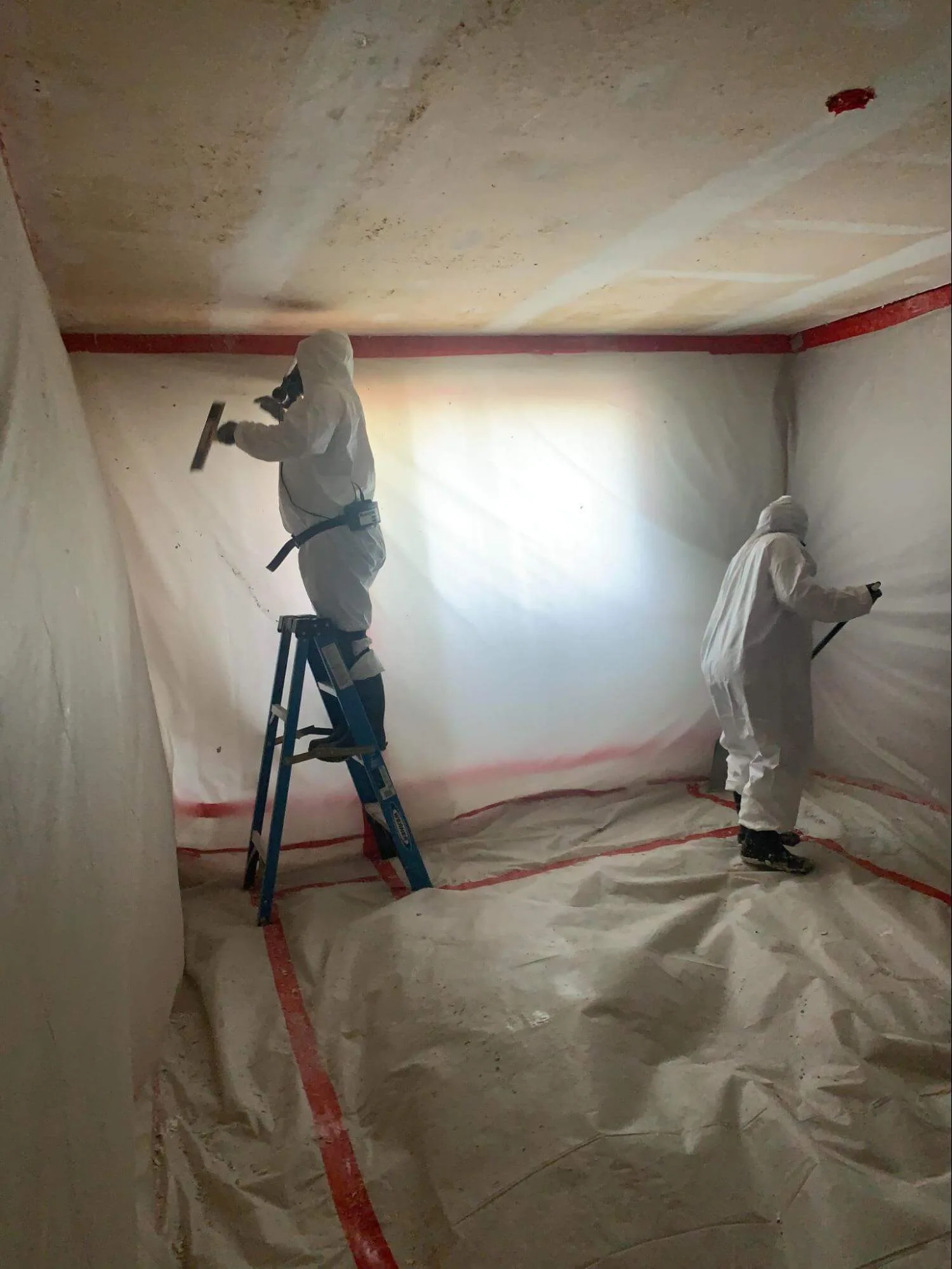 Workers removing popcorn ceiling in contained room